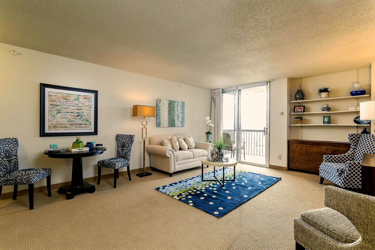 A cozy living room with a sofa, colorful rug, and natural light from a large window.