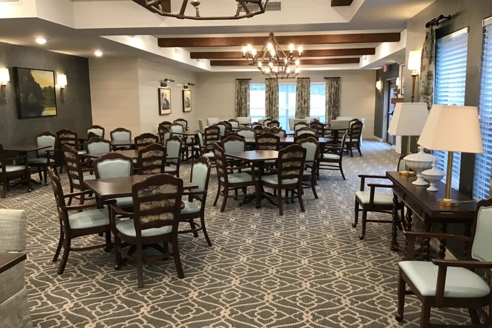 A spacious dining area with multiple tables and chairs, featuring chandeliers and decorative ceiling beams.