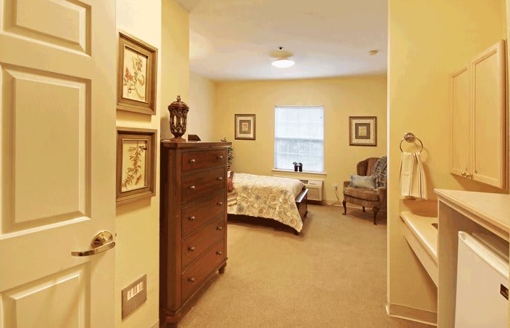 A cozy bedroom with warm lighting, featuring a bed, dresser, and armchair.