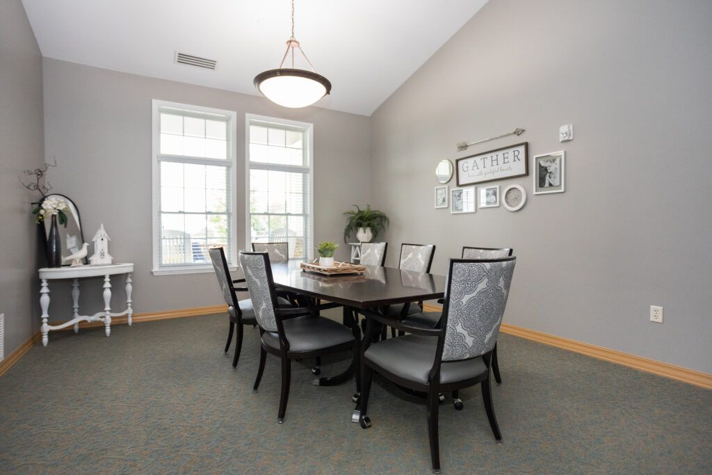 A modern dining room with a large table and elegant chairs, featuring ample natural light from two large windows.