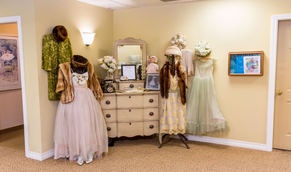 A display of vintage dresses and accessories on mannequins beside a vanity dresser with a mirror.