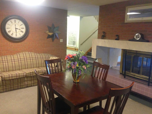 A cozy living and dining area featuring a wooden dining table adorned with flowers, surrounded by chairs, and a comfortable sofa in the background.