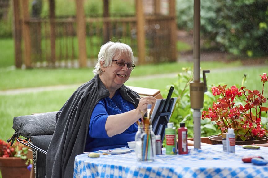 A woman painting at a table in a garden setting.