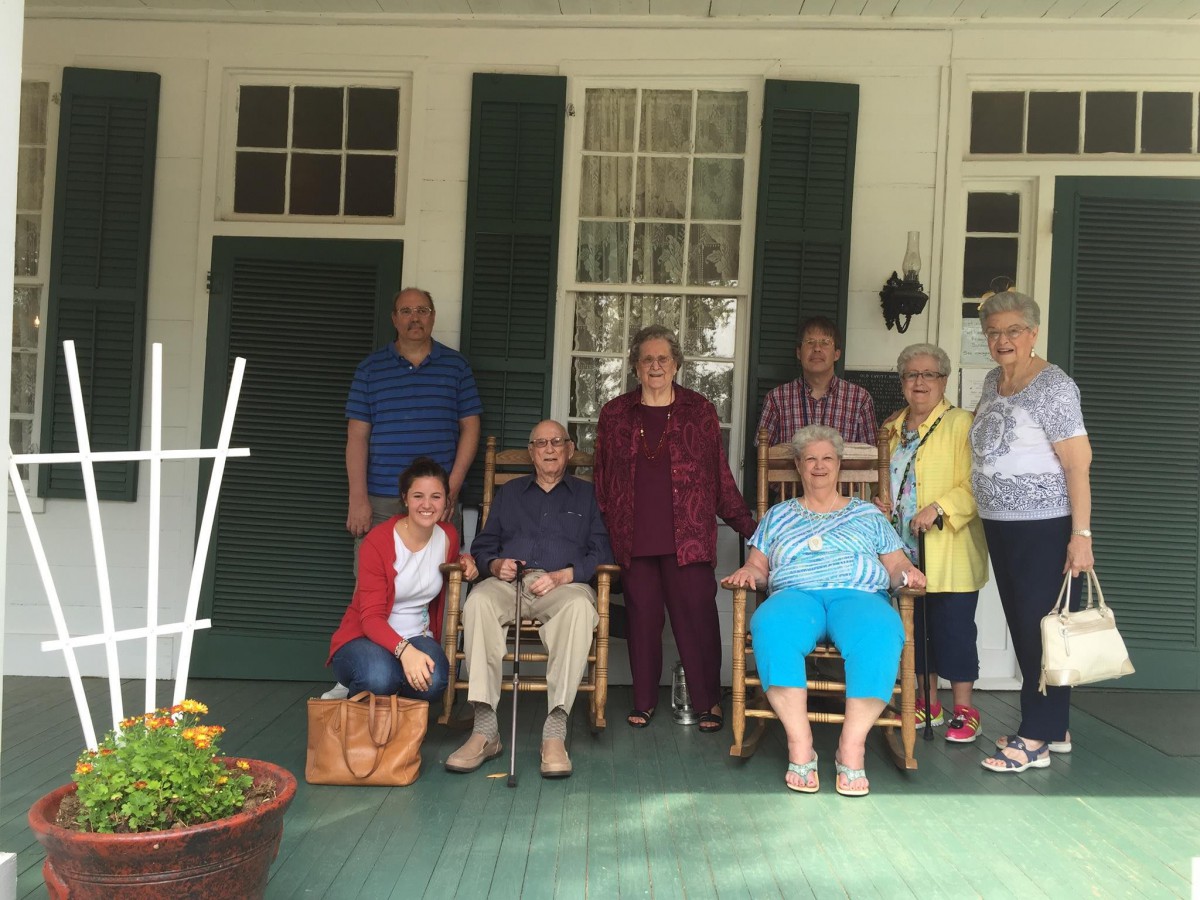 A group of people gathered on a porch, posing for a photo in casual attire.
