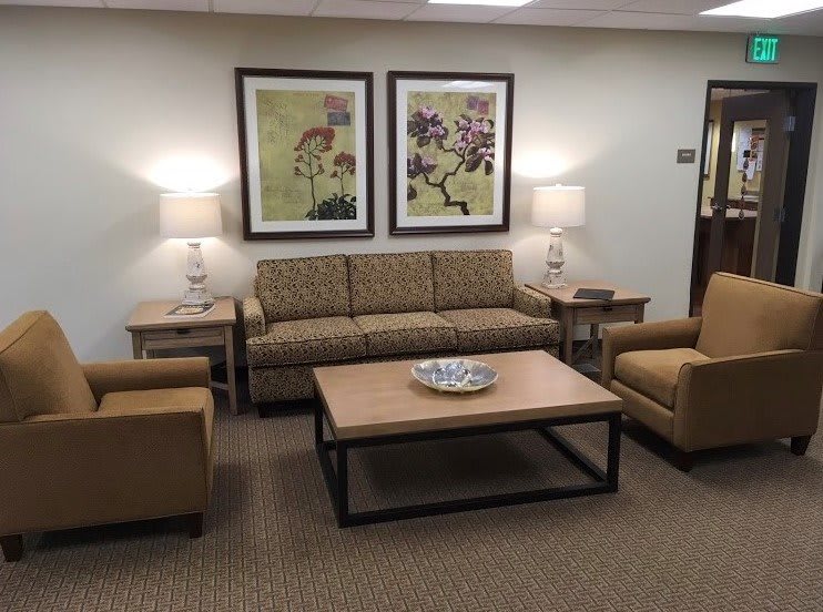 A cozy waiting room featuring a sofa, chairs, coffee table, and decorative artwork.