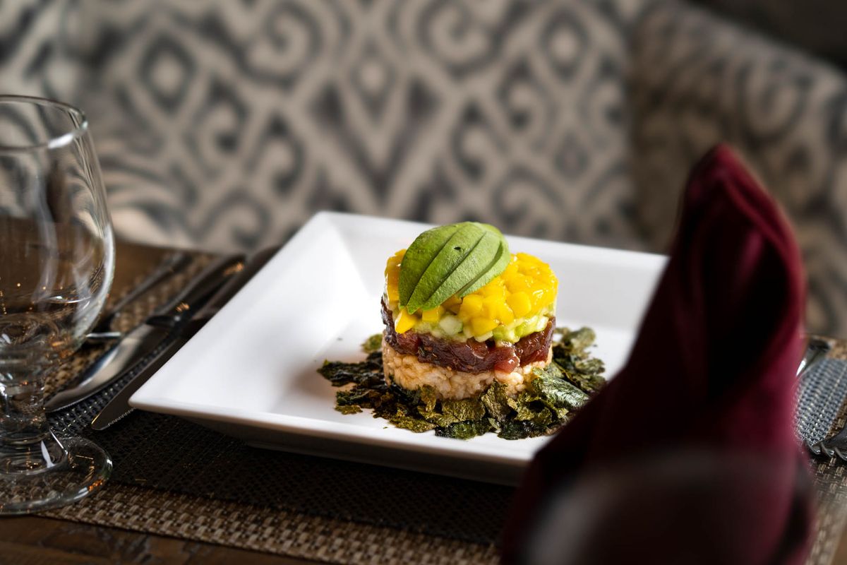 A beautifully plated gourmet dish featuring layers of avocado and mango.