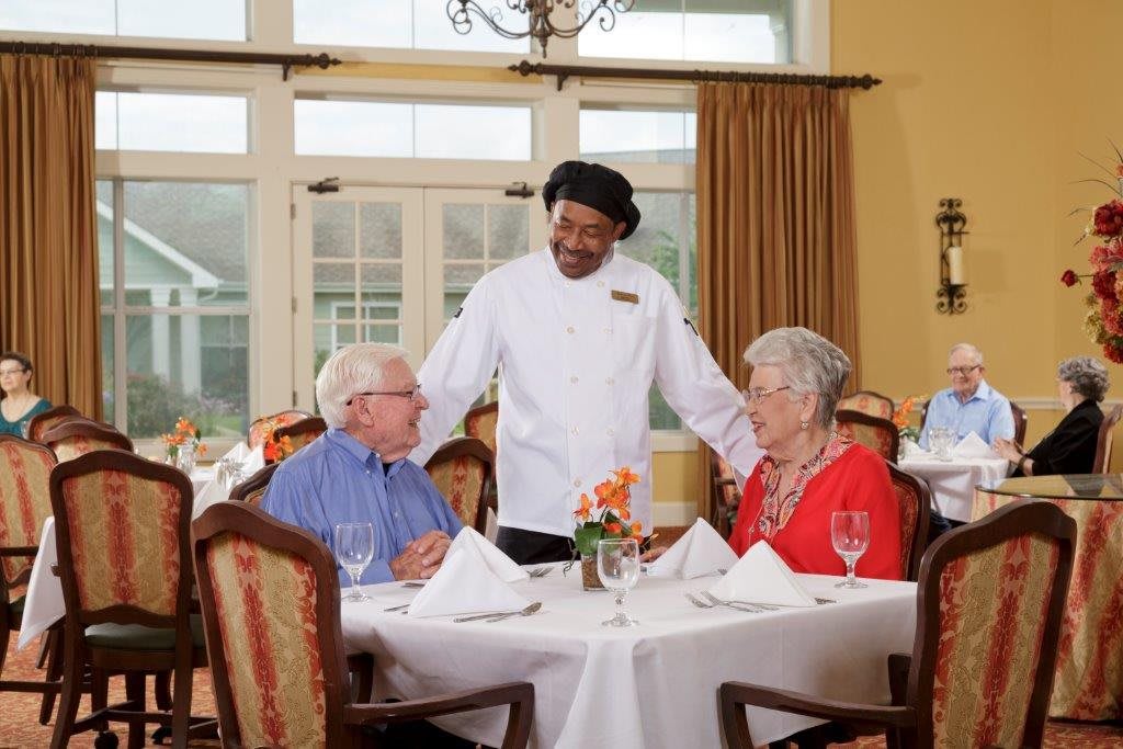 A chef engages in conversation with an elderly couple at a restaurant table.