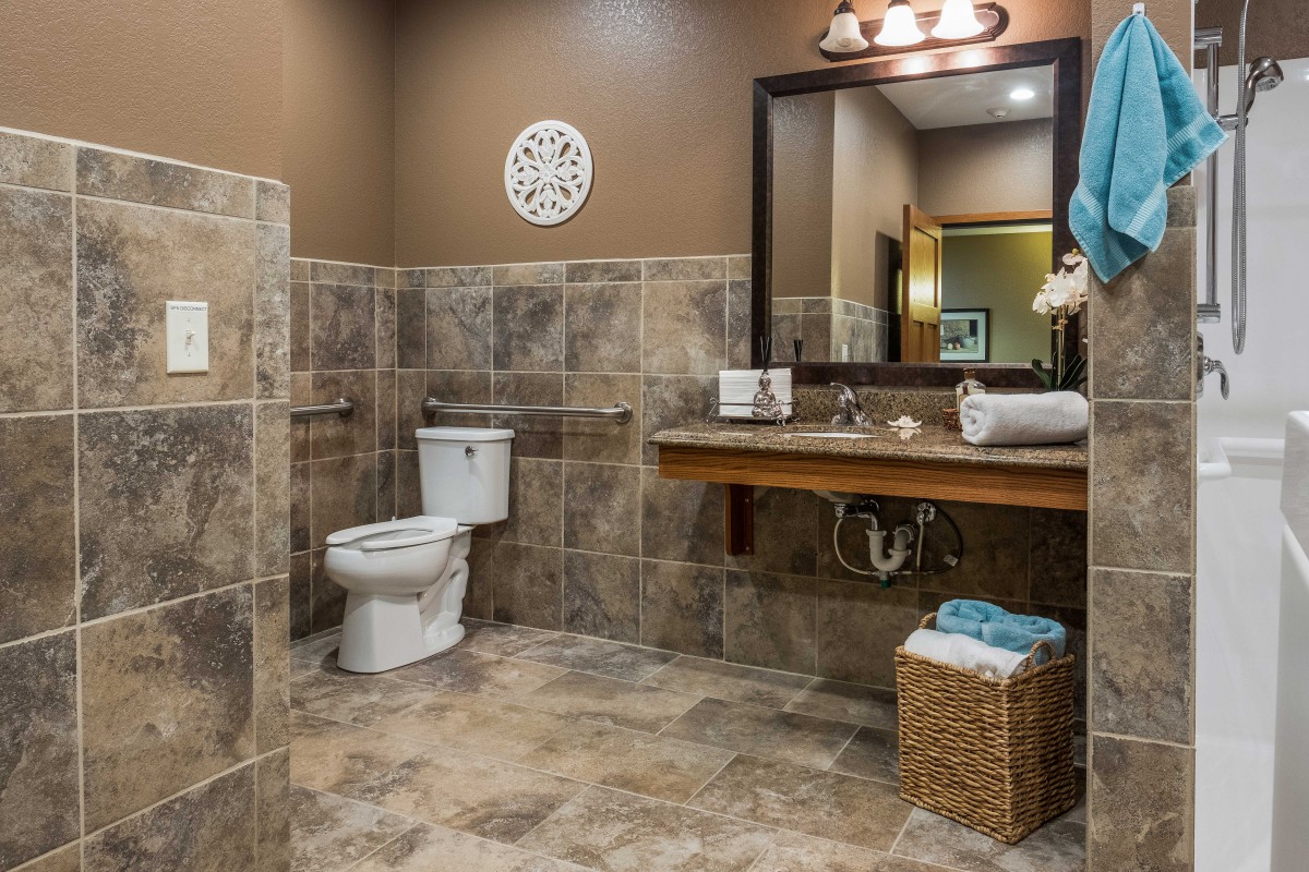 A modern bathroom with tiled flooring and walls, featuring a toilet, sink, and mirror.