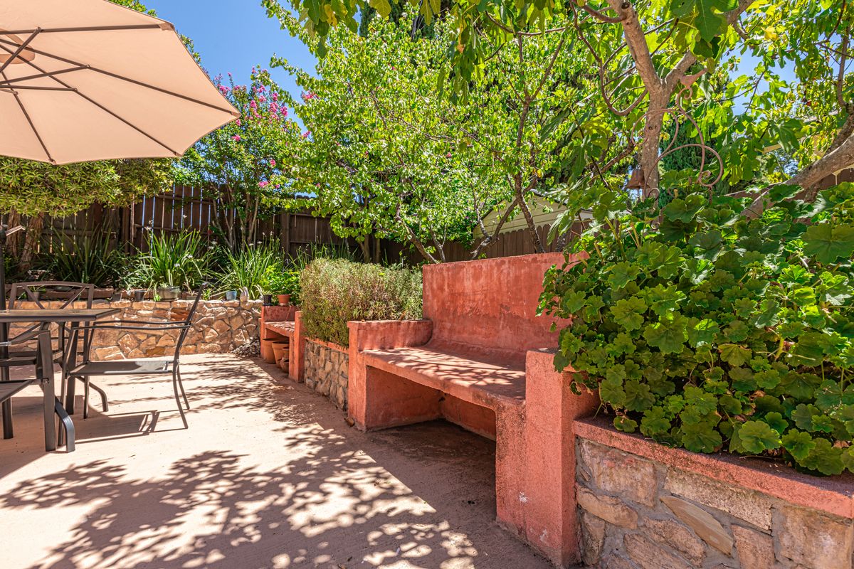 A sunny patio garden with a built-in bench surrounded by lush greenery.