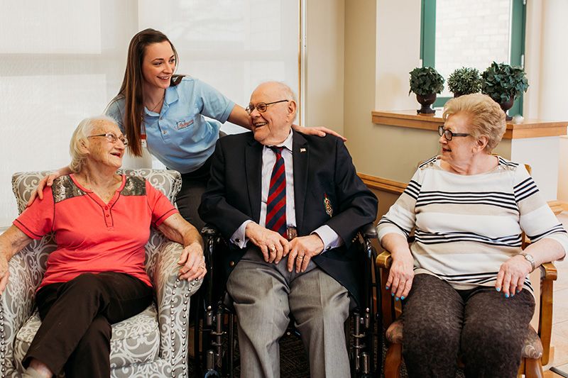 A caregiver interacting with seniors in a nursing home setting, all smiling and enjoying each other's company.