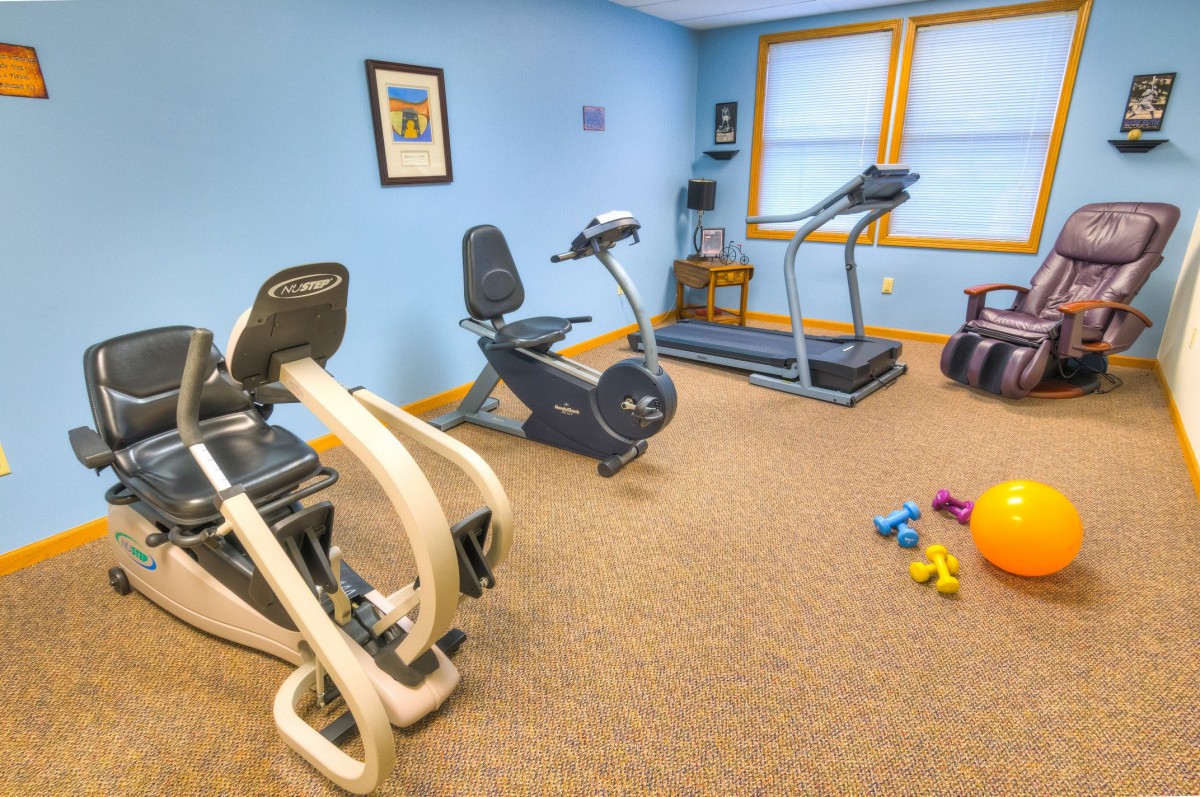 A small home gym with exercise equipment including a treadmill, stationary bikes, and dumbbells on the floor.