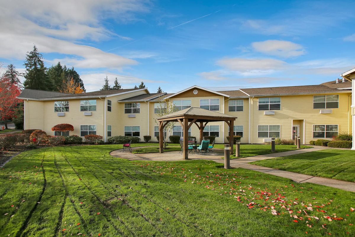 A two-story residential building with a gazebo in the foreground, set against a backdrop of blue sky and clouds.