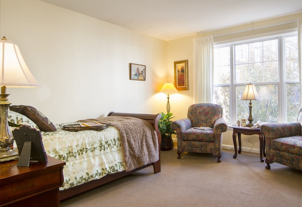 A cozy bedroom featuring a single bed, armchair, and a bright window with natural light.