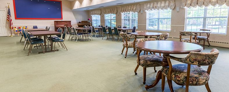 A spacious dining room with multiple tables and chairs, featuring large windows and a piano.