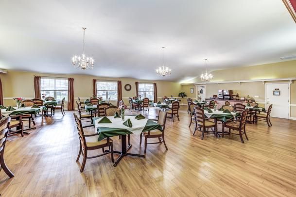 A spacious dining room with neatly arranged tables and chairs, featuring chandeliers and wood flooring.