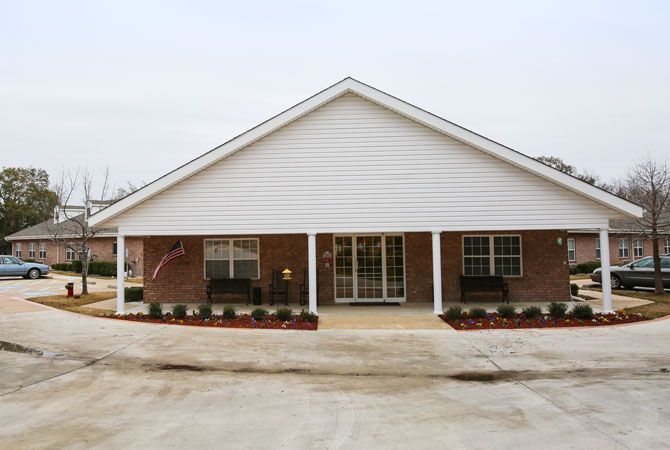 A single-story brick residential building with a covered front porch and landscaped yard.