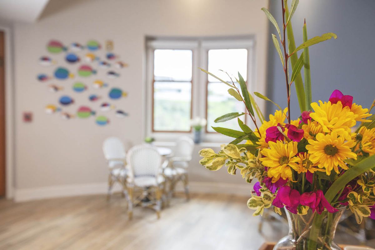 A cozy interior space with vibrant flowers in the foreground and a small dining area in the background.