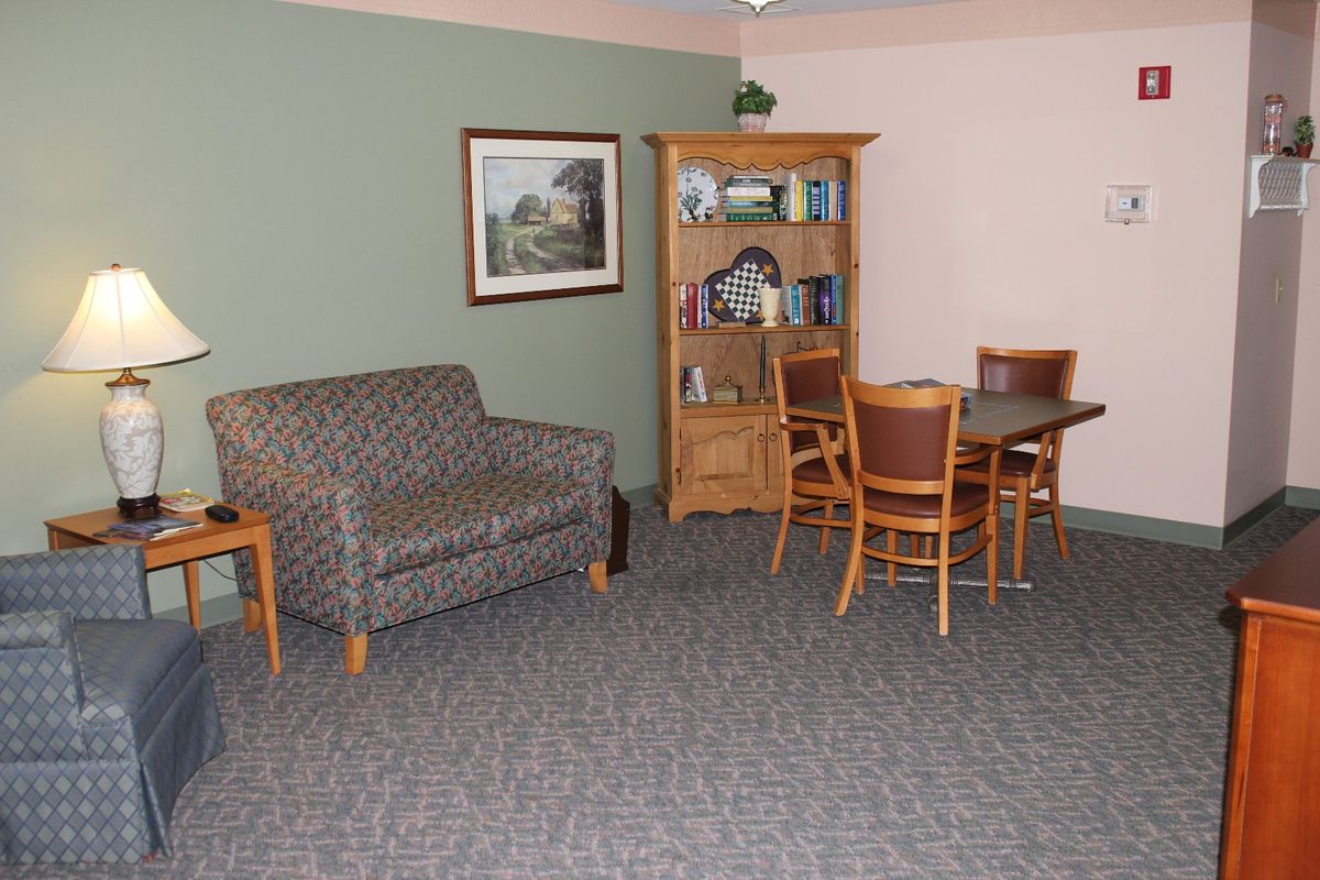A cozy living room with a patterned sofa, wooden bookshelf, and a dining table with chairs.