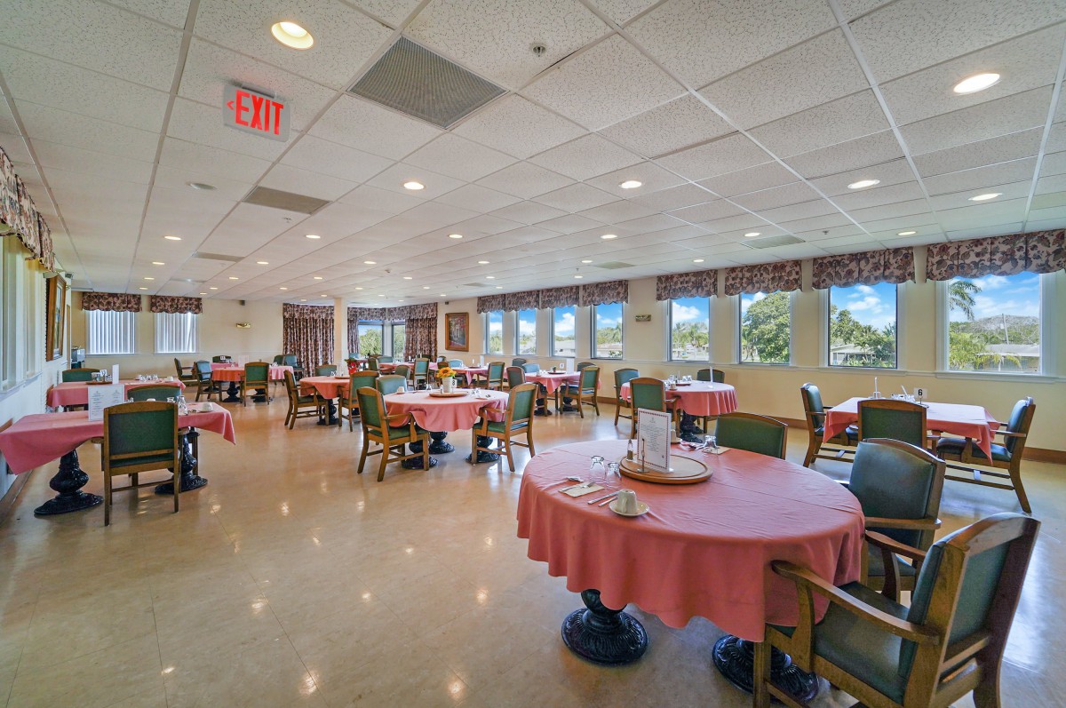A spacious dining room with neatly arranged tables and chairs, featuring large windows and bright lighting.