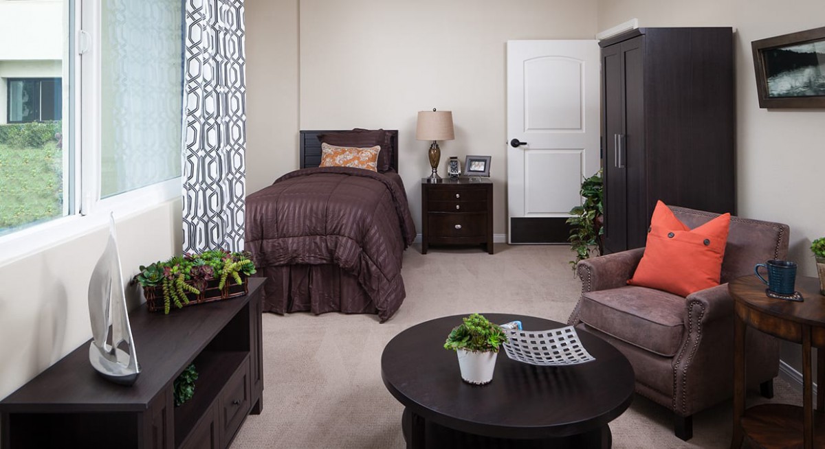 A cozy bedroom with modern decor, featuring a bed, nightstand, table with plants, and comfortable seating.