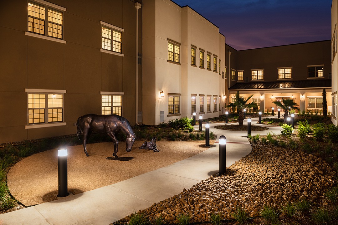A well-lit courtyard at night featuring a horse statue and surrounding building.