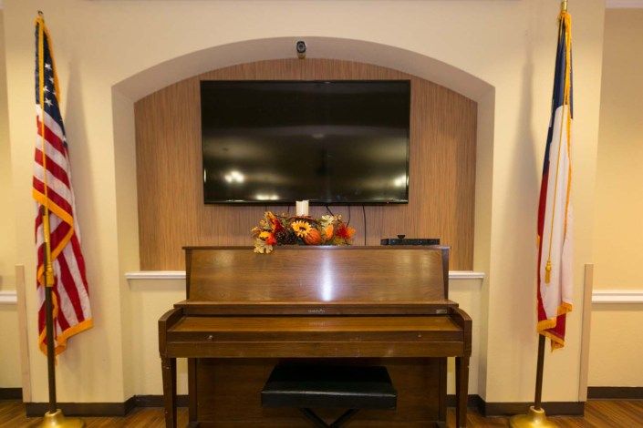 A room featuring a piano with autumn decorations, beneath a wall-mounted television within an arched alcove.