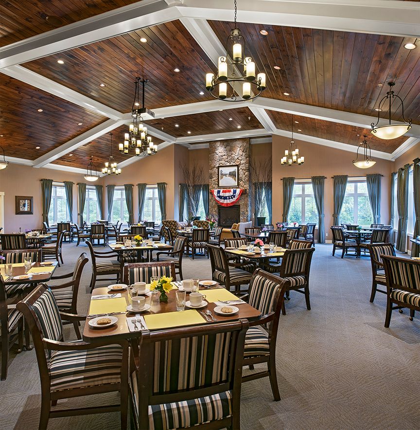 A spacious and elegantly designed dining hall featuring wooden furniture, large windows, and stylish chandeliers.