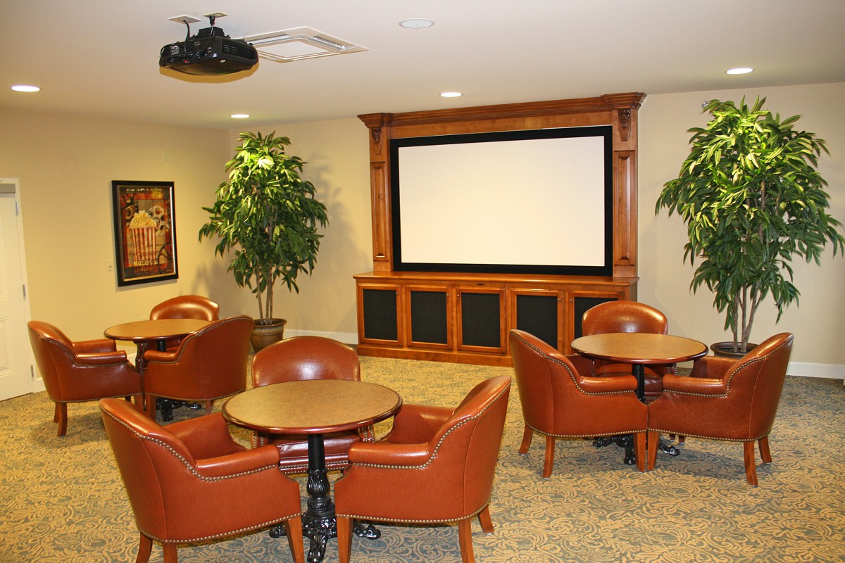 A conference room with tables, chairs, a projector screen, and decorative plants.