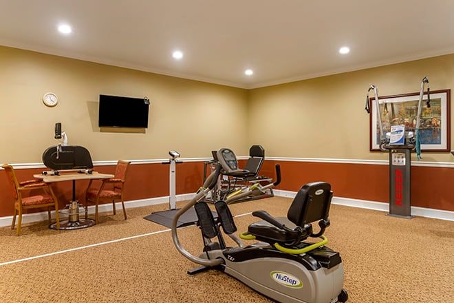 A well-lit gym room with a stationary bike and TV, featuring a small seating area.