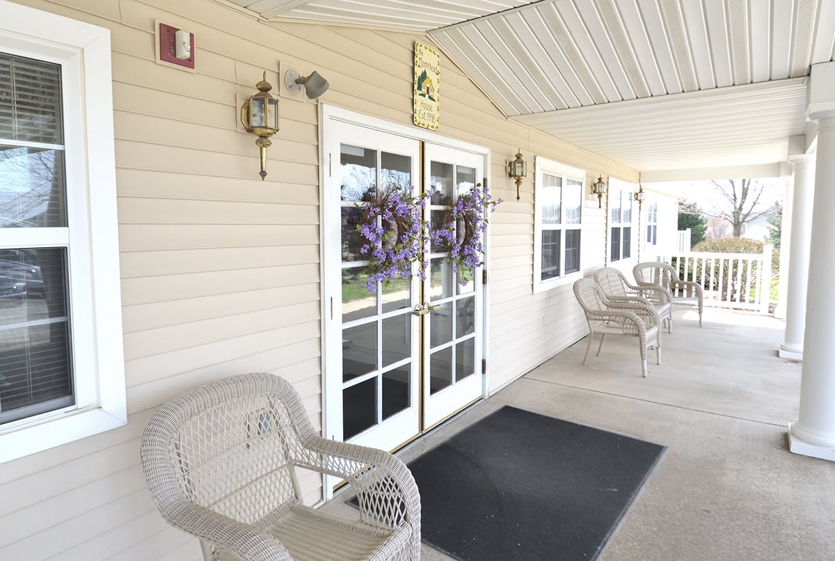 A cozy front porch entrance with white doors adorned with wreaths, surrounded by wicker chairs and decorative lighting.