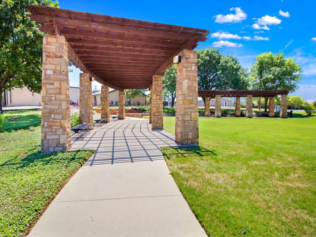 A scenic outdoor walkway with a wooden pergola and stone pillars under a clear blue sky.