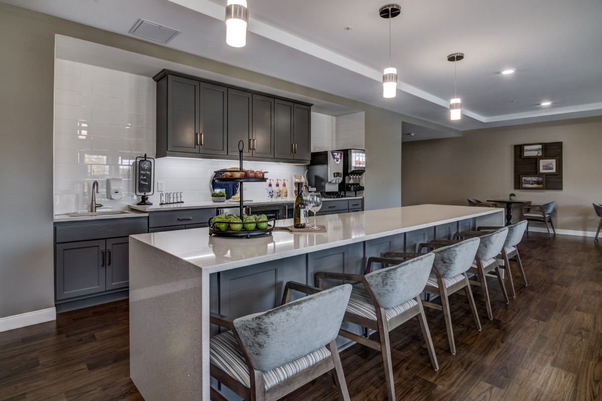 A modern kitchen with a long countertop and bar stools, featuring sleek cabinetry and stylish lighting.