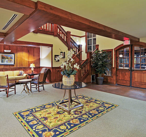 A cozy lobby area with wooden decor, featuring a seating arrangement, staircase, and decorative plants.