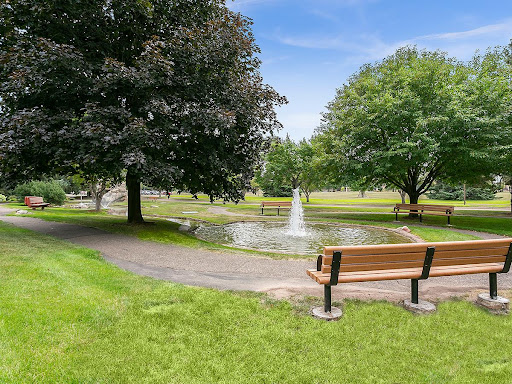 A serene park setting featuring a small fountain surrounded by lush greenery and benches.