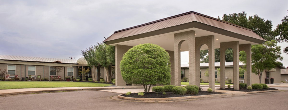 A modern building with a circular driveway and a neatly trimmed bush in the foreground.