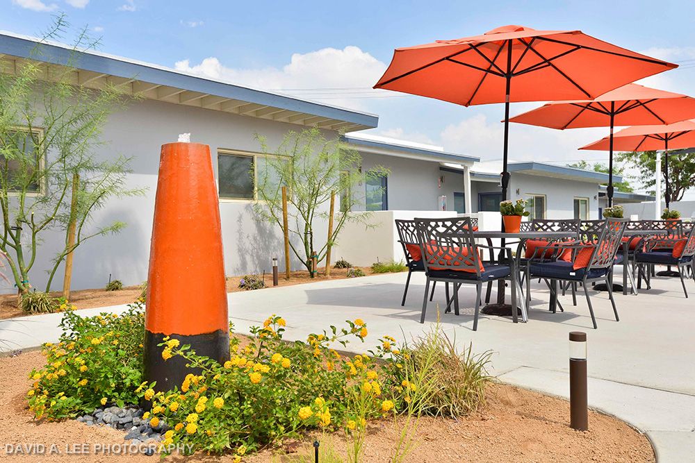 A well-designed patio with furniture and an orange umbrella, surrounded by garden landscaping.