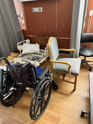 A room with a wheelchair, a chair, and a disassembled hospital bed.