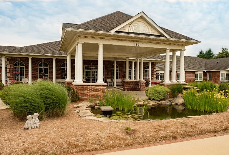 A charming house with a porch supported by white columns, surrounded by a well-maintained garden and a small pond.