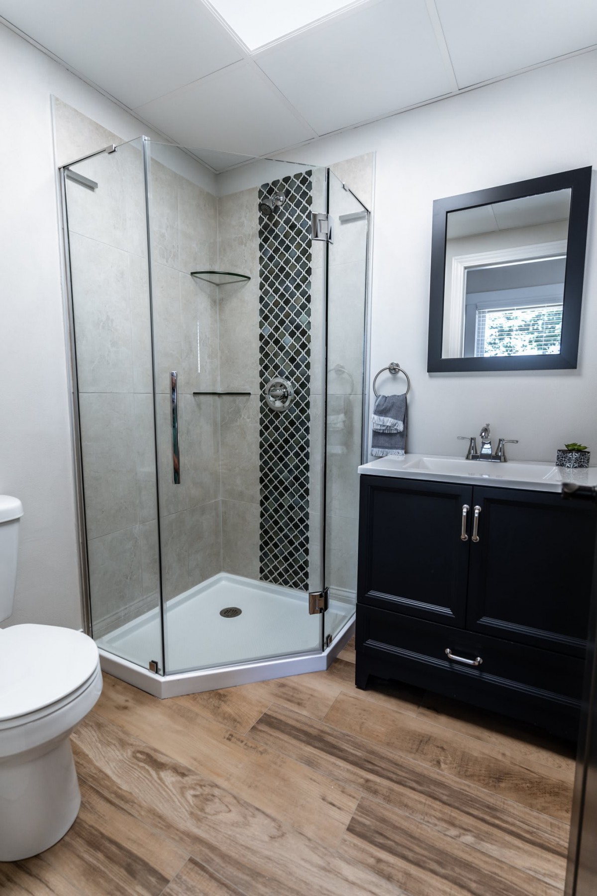 A modern bathroom featuring a glass-enclosed shower, a dark vanity with a sink and mirror, and tile flooring.