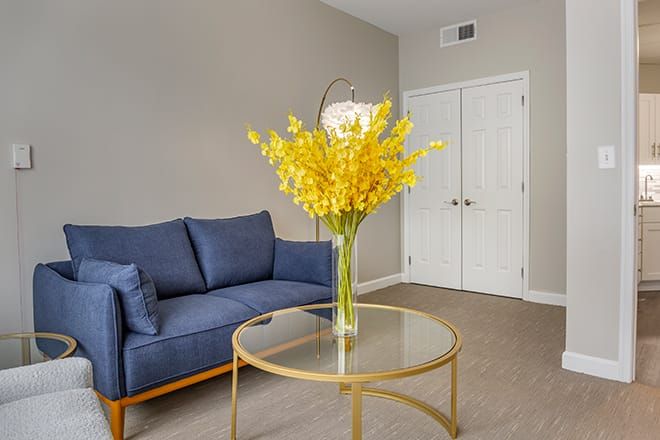 A modern living room with a blue sofa and a round glass table adorned with yellow flowers.