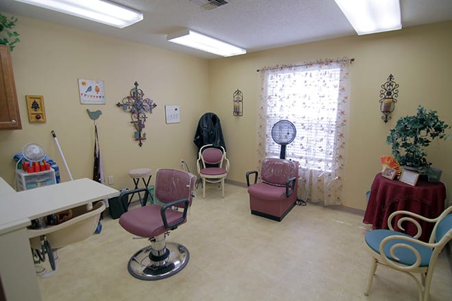 An interior view of a hair salon with various chairs, a hair dryer, and decorative items on the wall.