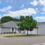 A suburban house with a driveway and attached garage, surrounded by greenery under a partly cloudy sky.