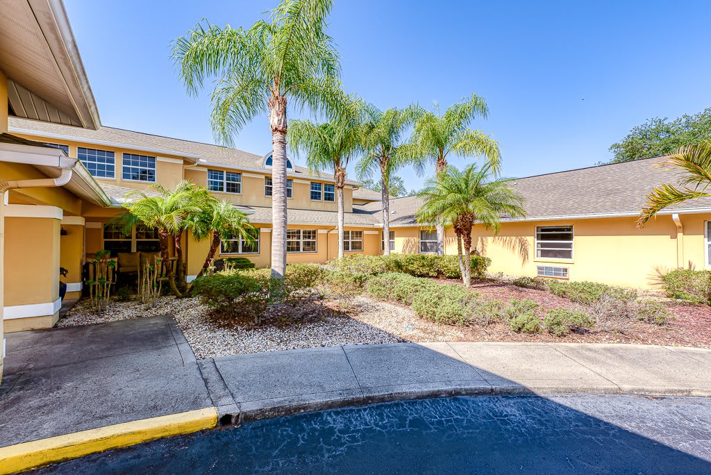 A sunny view of a yellow building surrounded by palm trees and landscaped gardens.