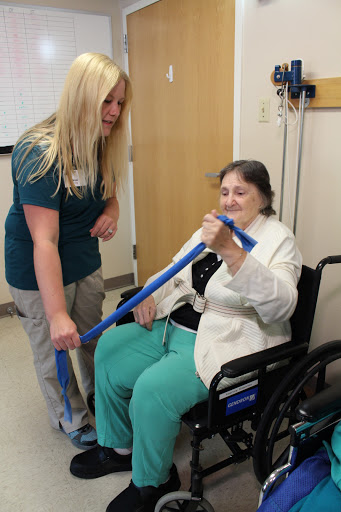 A healthcare professional assists an elderly patient in a wheelchair during a physical therapy session.