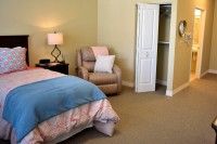 A cozy bedroom with a bed, armchair, lamp, and open closet door.