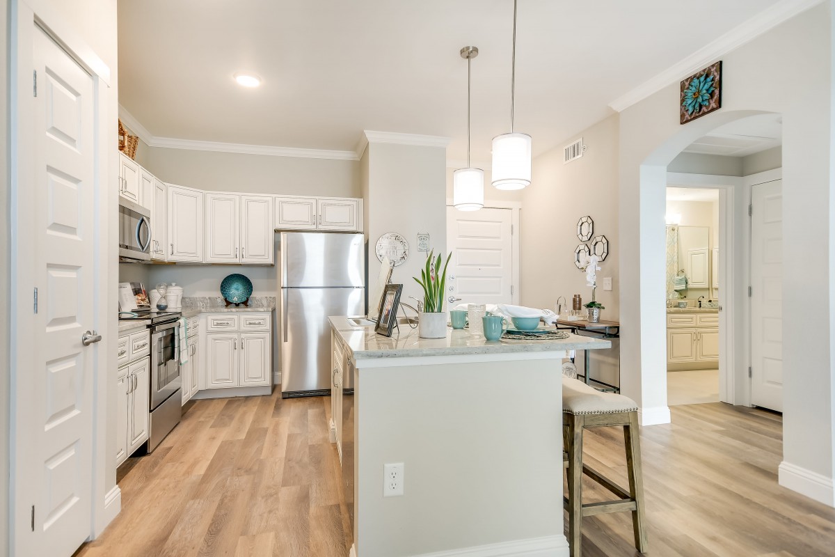 A modern kitchen with stainless steel appliances and white cabinetry, featuring pendant lighting and wood flooring.
