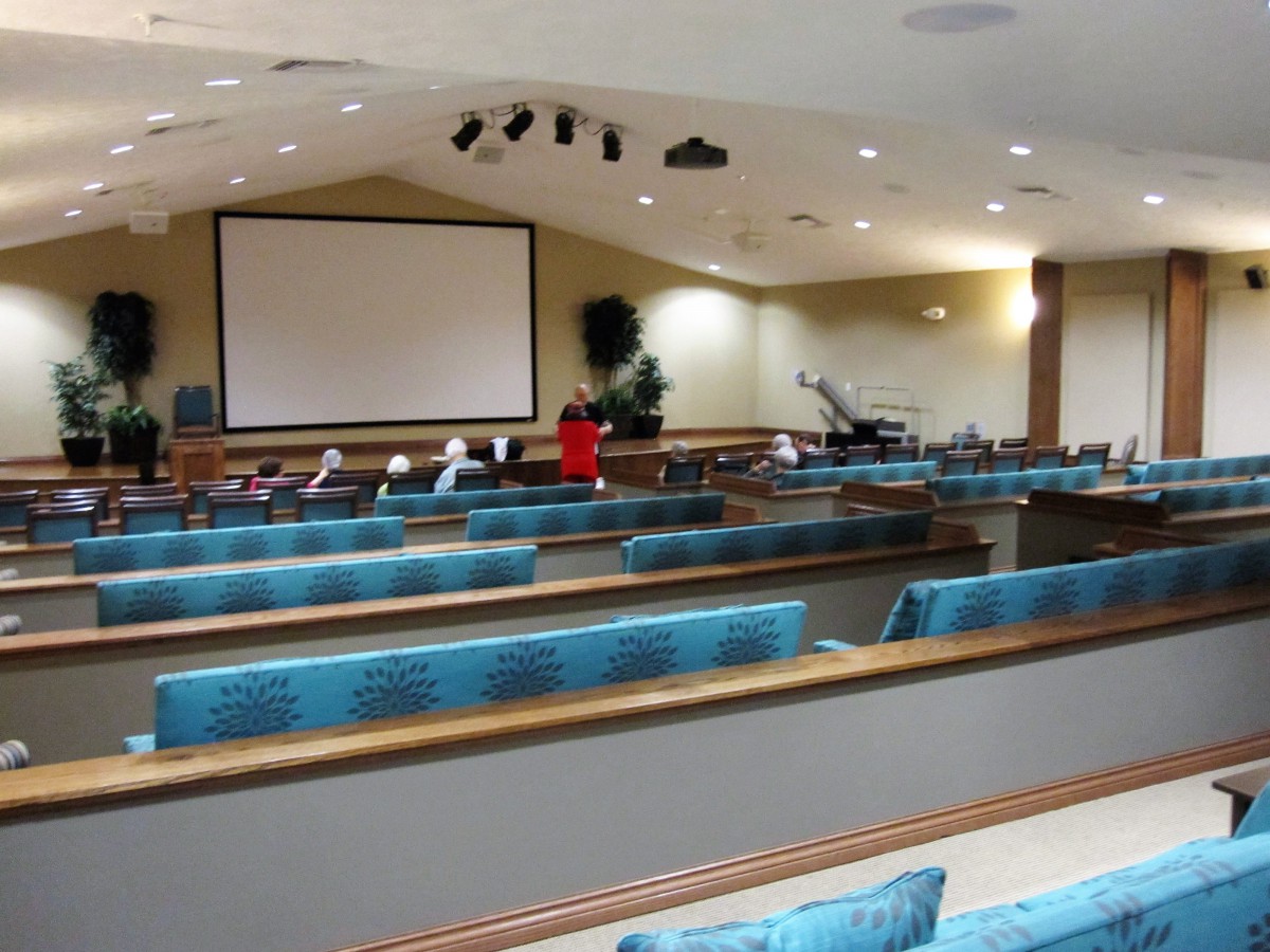 An interior view of a church auditorium with empty pews and a large projector screen.