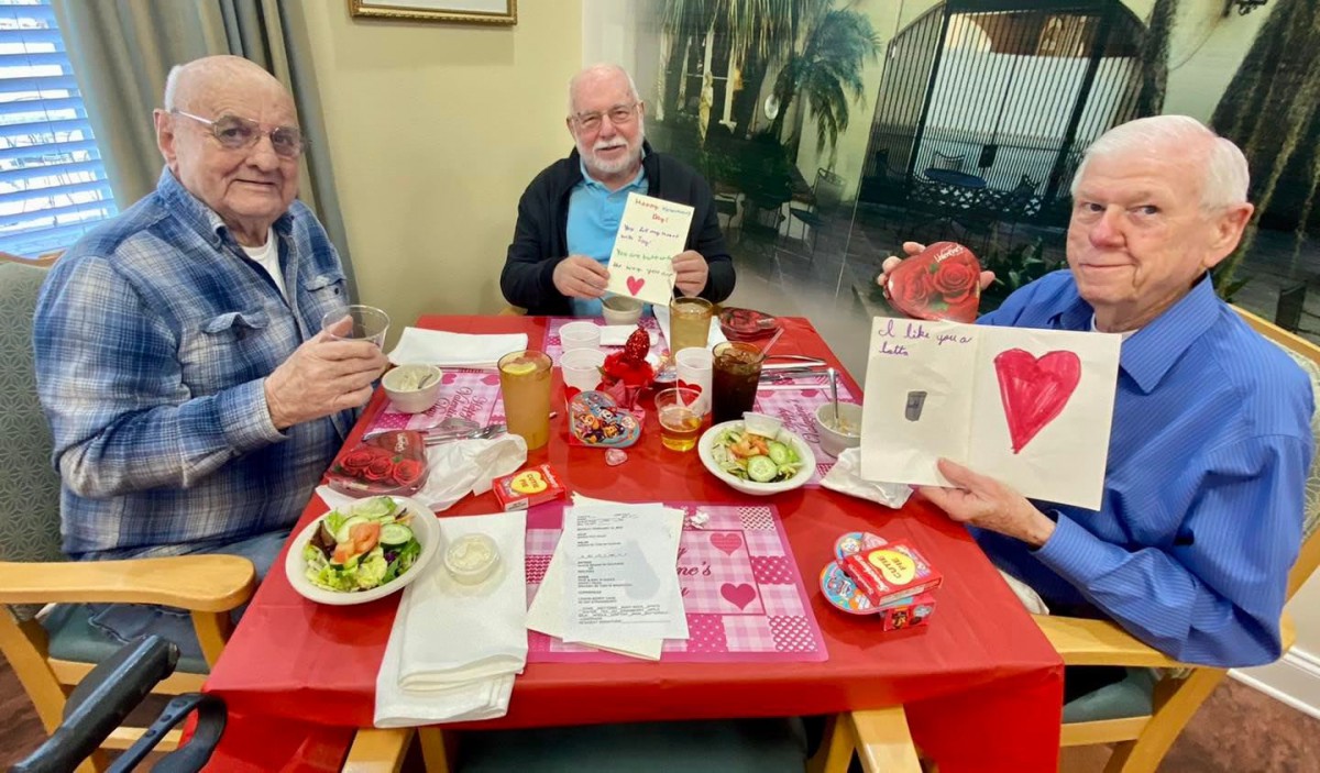 Elderly friends celebrate Valentine's Day with cards and a meal at a decorated table.