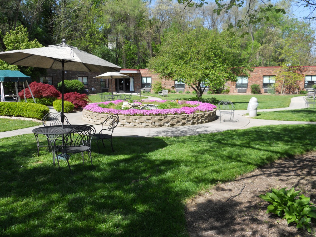A serene garden with a flower bed, patio furniture, and green surroundings.