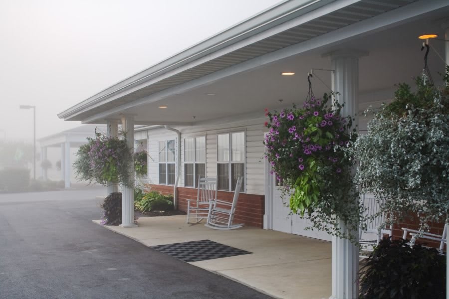 A building entrance with a covered porch, adorned with hanging plants and rocking chairs.